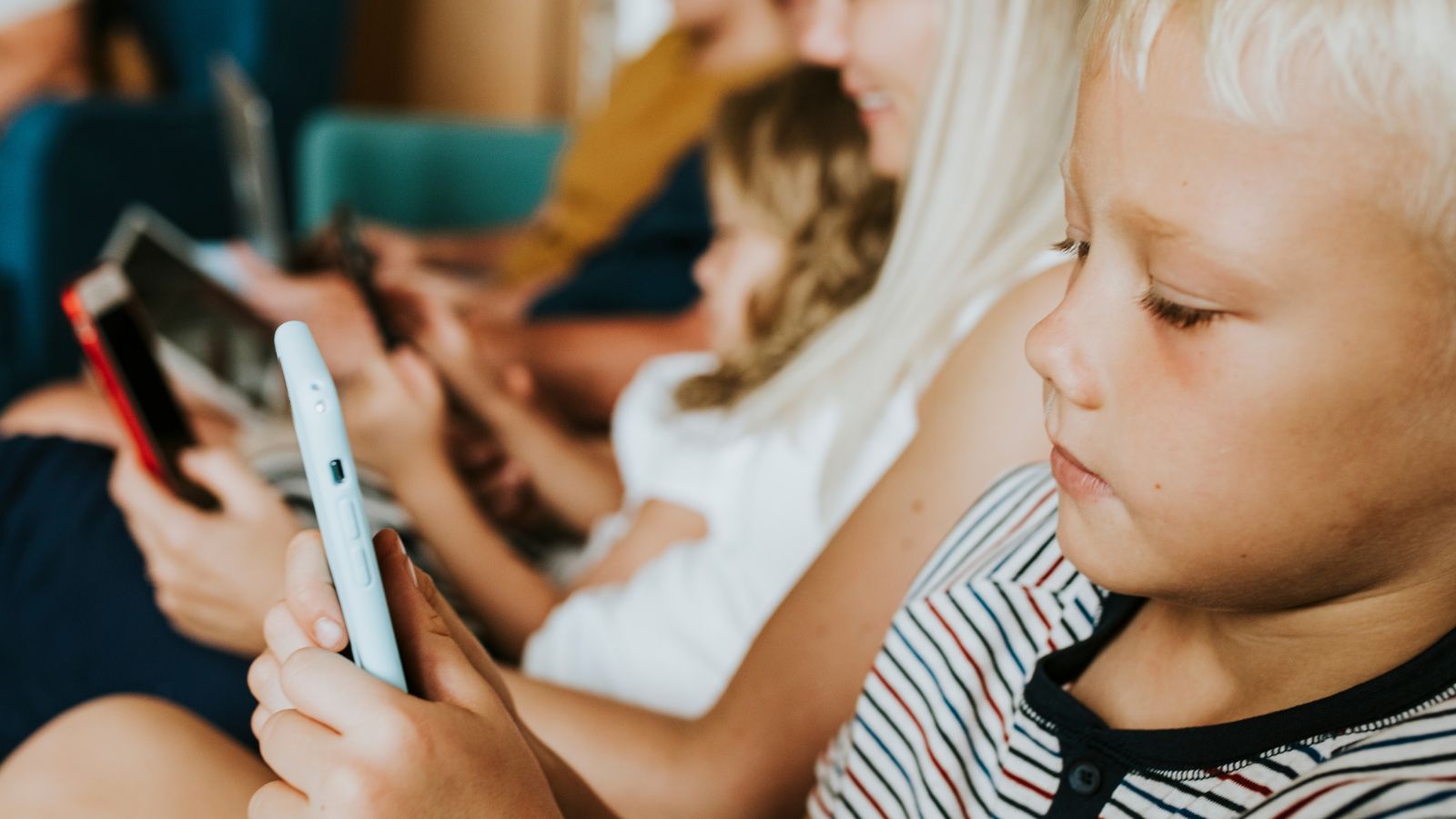 Criança usando celular ao lado da família