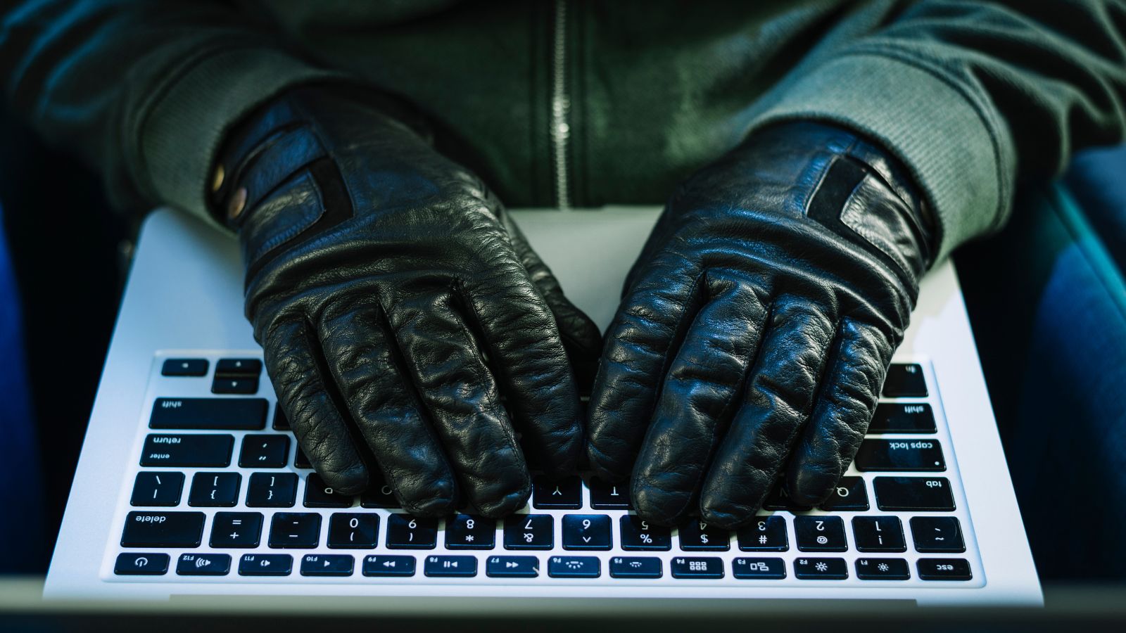 Homem com luvas pretas digitando em notebook