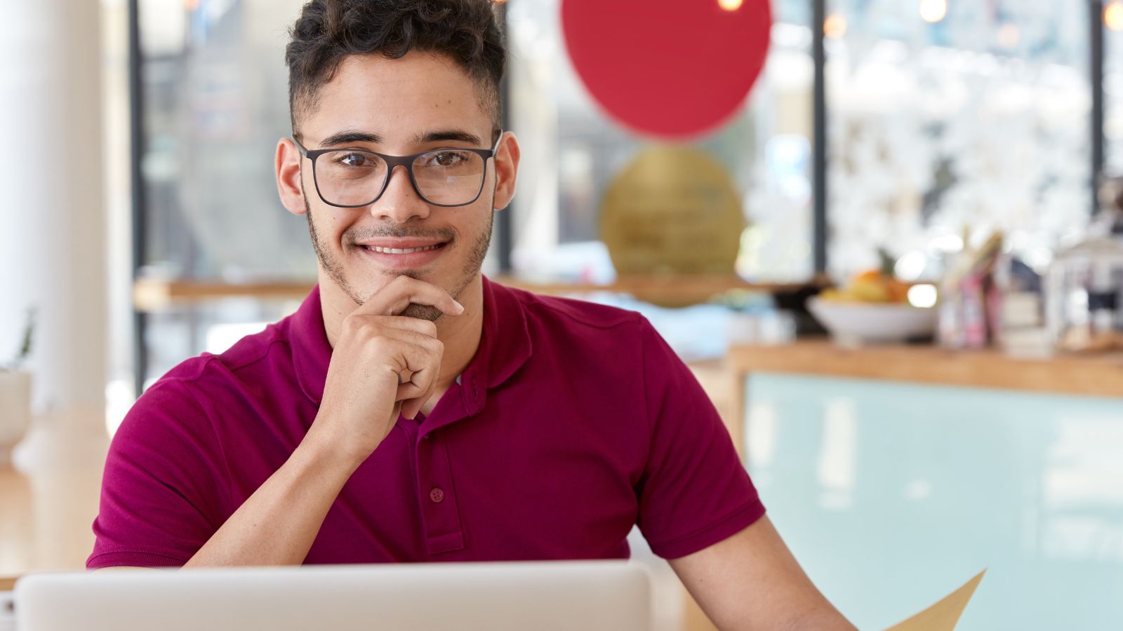 Jovem sentado em frente ao notebook com a mão no queixo