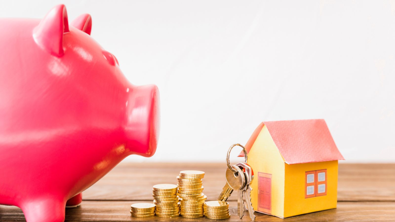 Porquinho, moedas e casa com chaves em cima de mesa